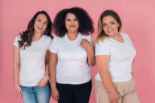 A group of girls in clean white t-shirts on a pink background. T-shirt mock-up for design on clothes