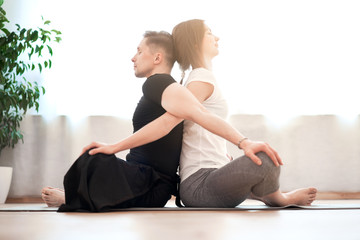 Fototapeta na wymiar Man and woman doing yoga sitting in lotus position on gray rug against background of window in room