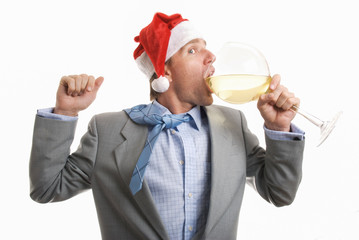 Partying businessman in Santa hat taking a big gulp from a large wine glass at the office holiday party