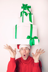 Man in Santa hat and red turtleneck balancing a tower of Christmas presents  with green ribbons on his head