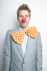 Businessman wearing red clown nose and big floppy tie looking at the camera with a funny expression 