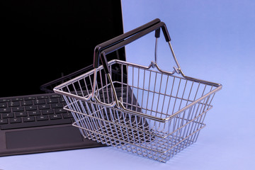 Internet shopping concept of a laptop computer with a mini shopping cart basket resting on the keyboard isolated against an blue background