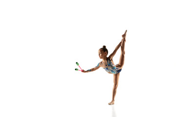 Little flexible girl isolated on white studio background. Little female model as a rhythmic gymnastics artist in bright leotard. Grace in motion, action and sport. Doing exercises with the maces.