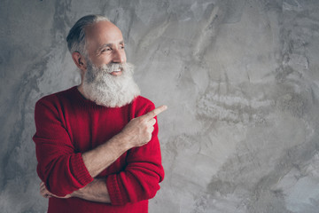 Photo of funny aged guy indicating finger empty space advising new product wear red knitted pullover hipster santa outfit isolated grey color wall background