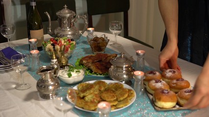 Festive family dinner. Traditional Hanukkah meal. On the table there is a jewish kosher symbolic fried food. Latkes, jelly-filled donuts, dairy produce, salad with cheese, chocolate Hanukkah gelt