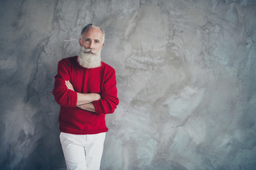 Photo of attractive aged guy holding hands crossed self-confident wear red knitted pullover white trousers cool hipster santa clothes isolated grey color concrete wall background