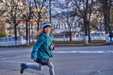 A teenager girl in glasses, in a knitted hat and coat is running across the square on a sunny...
