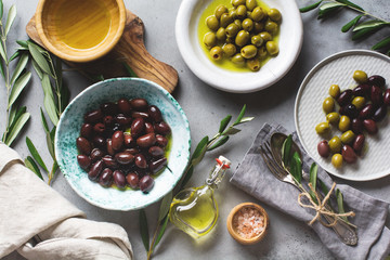 Several varieties of fresh olives in different ceramic plates on an old vintage gray table concrete background. Natural product concept. Rustic vintage set of cutlery. Top view, copy space.