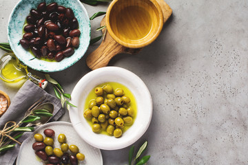 Several varieties of fresh olives in different ceramic plates on an old vintage gray table concrete background. Natural product concept. Rustic vintage set of cutlery. Top view, copy space.