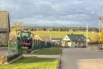 Village street. A tractor with a plow stands near a barn. Podlasie, Poland.