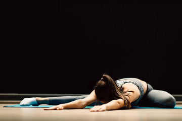 Fototapeta na wymiar Athletic girl stretching lying on rug in sports hall