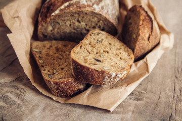Brown fresh bread with seeds are cut into pieces on old wood background. Top view, copy space