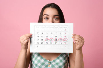Young woman holding calendar with marked menstrual cycle days on pink background - obrazy, fototapety, plakaty