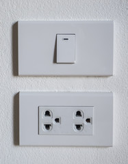 white plastic light switch with a single button and two electric plug wall affixed to a plain white wall.