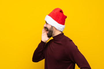 Fototapeta na wymiar Man with christmas hat over isolated yellow background shouting with mouth wide open to the lateral