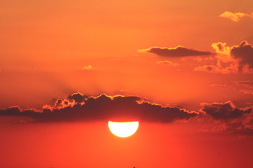 Red summer sun at sunset among the clouds.