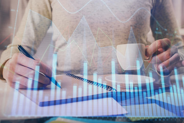 Forex chart hologram on hand taking notes background. Concept of analysis. Double exposure