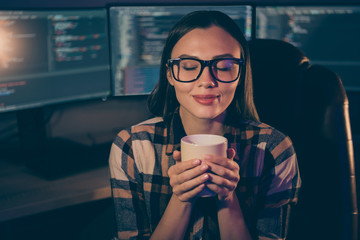 Photo of pleased satisfied cheerful joyful girl in spectacles enjoying aroma of freshly brewed coffee on the background of script java monitors