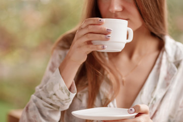 cup of coffee on the balcony. girl in the mountains. girl dressed in pajamas woke up in the morning and drinks coffee. girl is standing on balcony with cup of tea