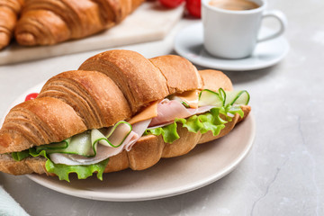 Tasty croissant sandwich with ham and cucumber on light table, closeup