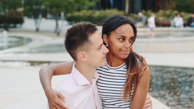 Handsome man and attractive black woman having date in a modern city park. They talking and man showing her something around.
