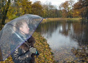 woman under a transparent umbrella on a cloudy autumn day on the lake shore..