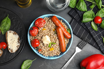 Tasty buckwheat porridge with sausages on dark grey table, flat lay