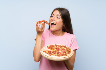 Pretty young girl holding a pizza over isolated blue wall