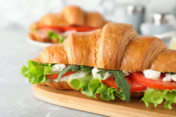 Tasty croissant sandwich with feta cheese and tomato on light grey marble table, closeup