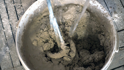 stream of water is poured into a bucket with a construction mixer and plaster