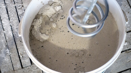 construction mixer (out of focus, rotates) is lowered into a bucket of liquid stucco