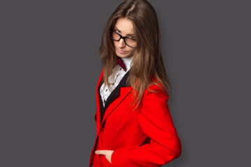 angry girl in white shirt, black vest and red jacket with Burgundy bow tie and classic black pants office style and glasses on gray background