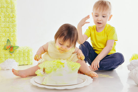 a little girl and boy eats cake with her hands on the bacfground of fireplace. The babys was covered in food. birthday party