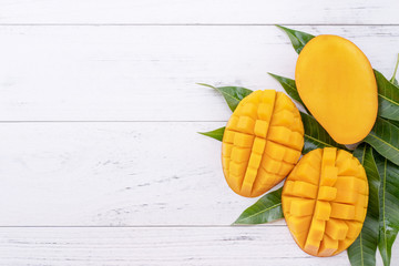 Beautiful chopped ripe mango with green leaves on bright white color wooden background, top view, flat lay, copy space. Tropical fruit design concept.