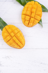 Beautiful chopped ripe mango with green leaves on bright white color wooden background, top view, flat lay, copy space. Tropical fruit design concept.