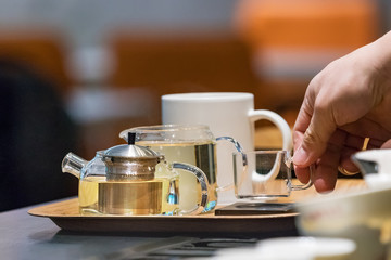 Barista male hands placing a glass cup on a tray with teapots at a coffe shop counter in Busan, South Korea.