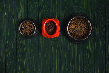 top view of bowls with pet food in row on green wooden surface with copy space