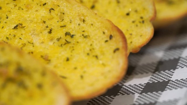 Garlic bread surface in macro or close up. Dolly shot, sliding camera move. Garlic Bread usually a baguette or sour dough like a ciabatta.