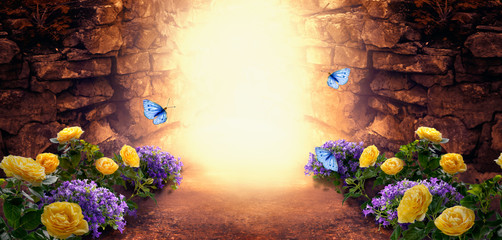 Photo background with magical trail leading through stone dungeon grotto cave towards mystical glow, fantastic bluebell, yellow rose flower, flying blue butterflies. Fairytale tranquil fantasy scene.