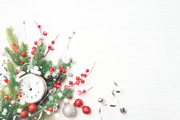 Christmas clock, fir branches and berries on white wooden background. New Year greeting card.