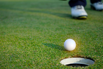 White golf ball near hole on green grass.