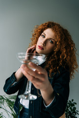 beautiful stylish redhead woman posing with glass on grey