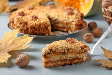 Homemade pumpkin pie with cinnamon and walnuts on a plate, with a slice of the pie cut out, on a light blue background, horizontal orientation