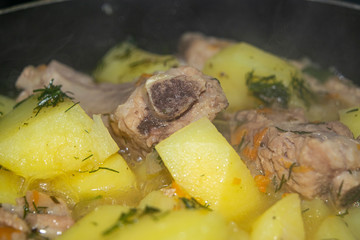Stewed pork ribs with potatoes, onions, carrots and dill in a saucepan. Close up. Traditional recipe. Home cooking.