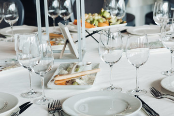 View over wedding table covered with white tablecloth with empty glasses, plates and utensils. Snacks are served on the table.
