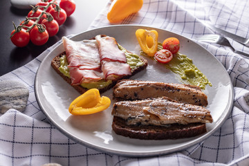 Homemade smoked herring and schwarzwald ham sandwiches with rye bread on light grey plate, top view 