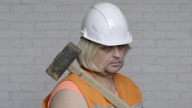 masculine woman in helmet and with sledgehammer is proud of her profession.
