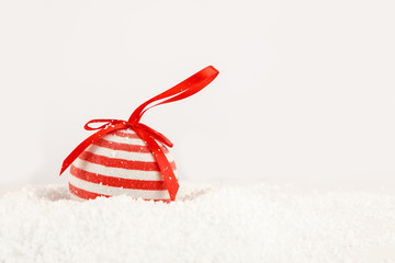 Red christmas ball with white dots and red ribbon in heap of fake snow on white background