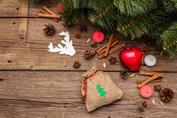 Spirit Christmas background. Gift in sack, New Year tree, apple, candles, spices, deer, cones. Nature decorations, vintage wooden boards