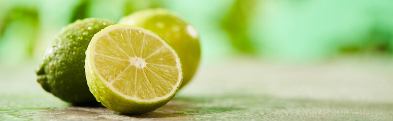 panoramic shot of whole and cut limes with drops on marble surface